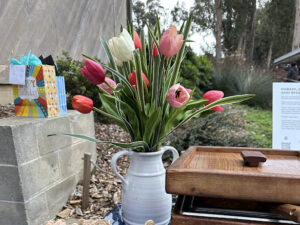 A white ceramic vase holds a bouquet of pink, red, and white tulips on a party table. Gifts and greenery are visible in the background.